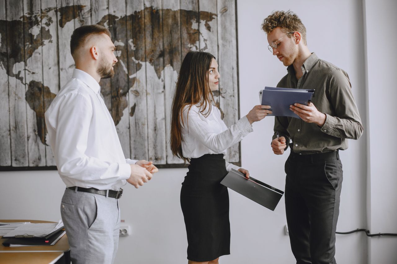 about-me-01 Three young professionals discussing documents in a modern office space.